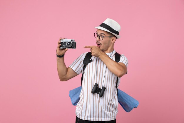 Front view male tourist holding camera on a pink wall emotion tourist color