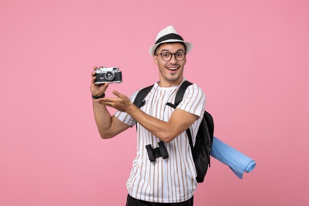 Вид спереди мужской турист, держащий камеру на розовой стене эмоции туристического цвета
