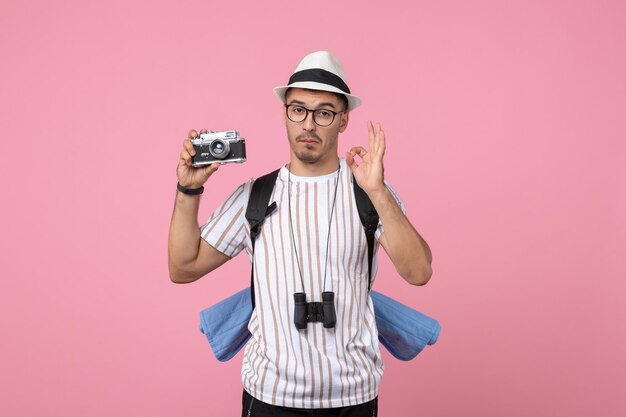 Front view male tourist holding camera on pink wall tourist emotion color