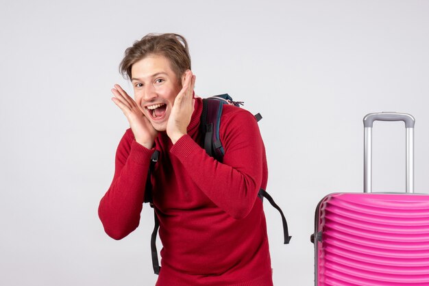 Front view of male tourist with backpack feeling happy on white wall