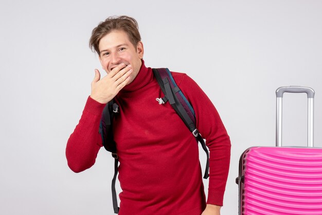 Front view of male tourist with backpack laughing on white wall