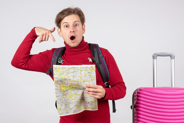 Вид спереди мужского туриста с рюкзаком и картой на белой стене