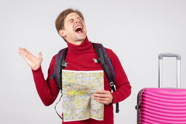 Front view of male tourist with backpack and map on white wall