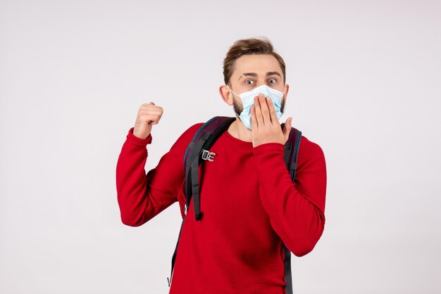 Front view male tourist with backpack in sterile mask on white wall