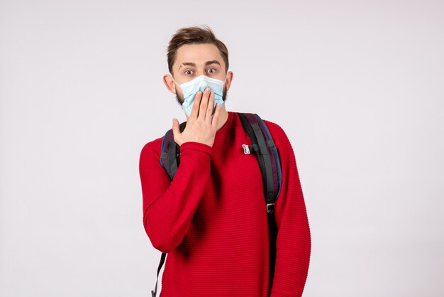 Front view male tourist with backpack in sterile mask on white wall