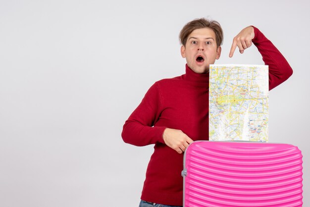 Front view of male tourist with map and pink bag on the white wall