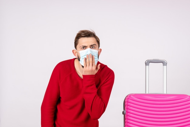 Turista maschio vista frontale con borsa rosa in maschera sul muro bianco