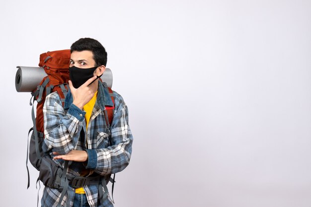 Front view male traveler with backpack and mask putting hand on his chin