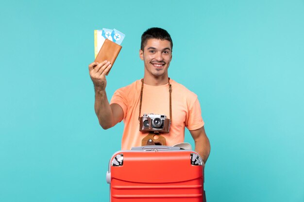 Front view male in vacation holding his tickets on blue