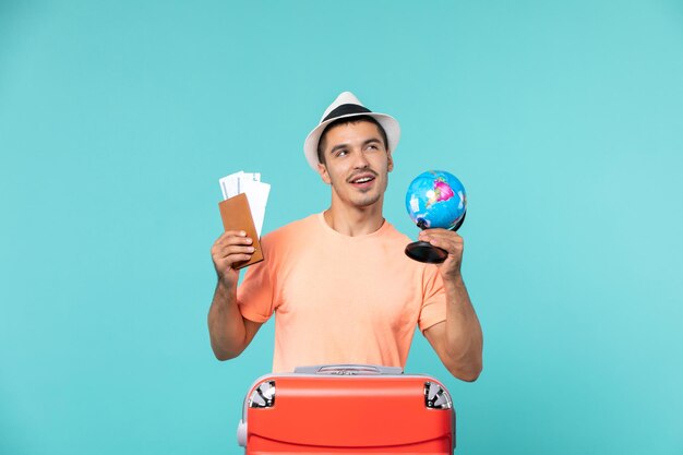 Front view male in vacation holding little globe and tickets on blue