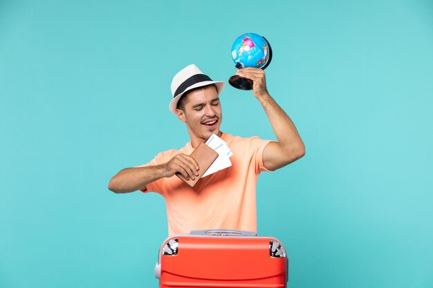 Front view male in vacation holding little globe and tickets on blue