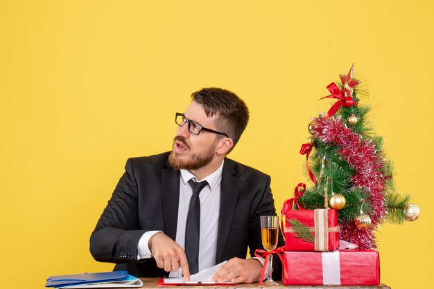 Вид спереди мужчина-работник за столом с подарками и рождественской елкой на желтом