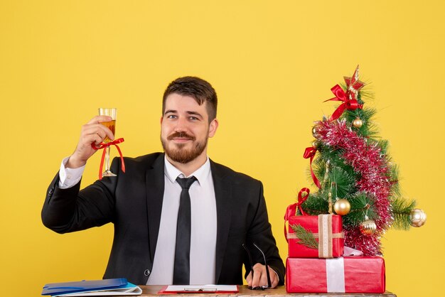 노란색에 선물과 크리스마스 트리와 그의 테이블 뒤에 전면보기 남성 노동자