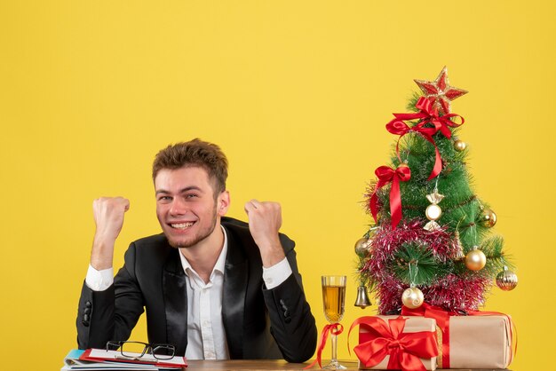 Front view male worker behind his working place with presents rejoicing on yellow 