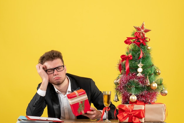 Front view male worker behind his working place with presents on the yellow 