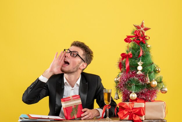 Front view male worker behind his working place with presents on yellow 