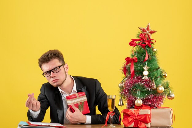 Front view male worker behind his working place with presents on yellow 