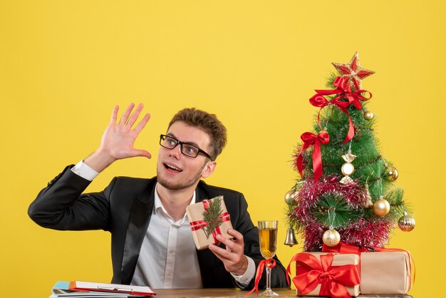 Front view male worker behind his working place with presents on yellow 