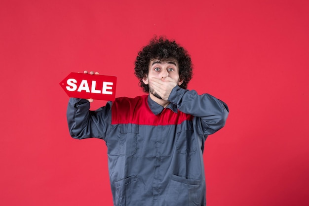 Front view male worker holding red sale nameplate on red background mechanic house color job worker uniform instruments photo