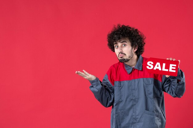 Front view male worker holding red sale nameplate on red background mechanic photo house color shopping job worker uniform instrument