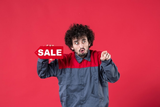 Front view male worker holding red sale nameplate on red background mechanic photo house job worker uniform instrument color shopping