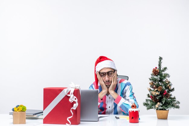 ラップトップで彼の場所に座っている正面図の男性労働者は疲れた仕事の感情のオフィスのクリスマスを感じています