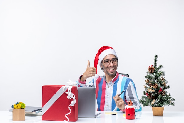 Вид спереди мужчина-работник, сидящий на своем месте с ноутбуком и файлами, позирующий в офисе, рождественские эмоции