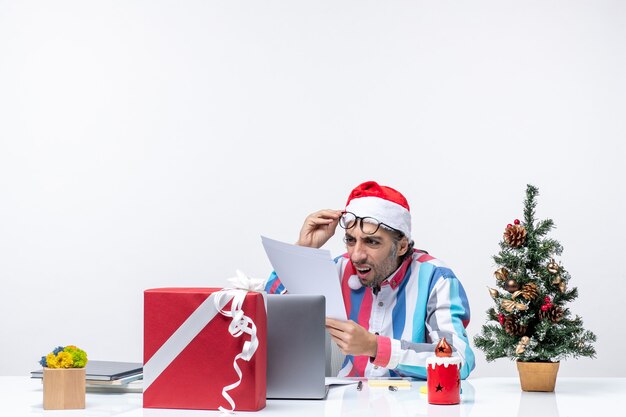 ドキュメントオフィスの仕事の感情のクリスマスで作業ラップトップで彼の場所に座っている正面図の男性労働者