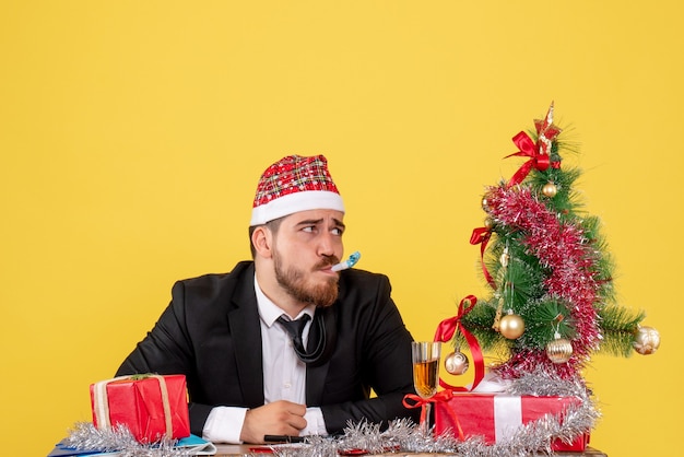 Front view male worker sitting behind his table with presents on yellow 