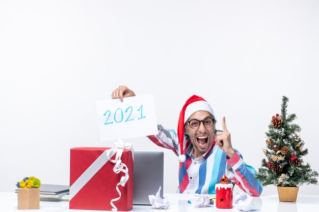 Front view male worker sitting in his working place excited holding paper sheet with number 2021, new year concept