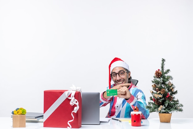 緑の銀行カードのオフィスの感情のクリスマスのお金の仕事の仕事を保持している彼の職場に座っている正面図の男性労働者