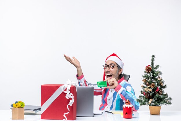 Вид спереди мужчина-работник сидит на своем рабочем месте, держа зеленую банковскую карту, офисную работу, эмоции, рождественские деньги