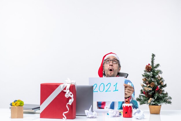 Front view male worker sitting in his working place holding note with writing new year office xmas new year