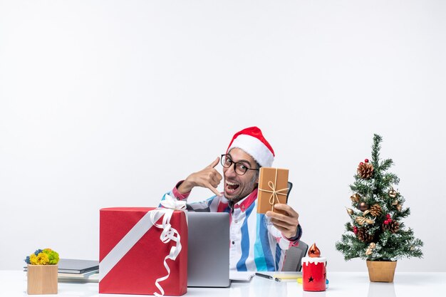 パッケージクリスマスの仕事の休日の感情のオフィスを保持している彼の職場に座っている正面図の男性労働者