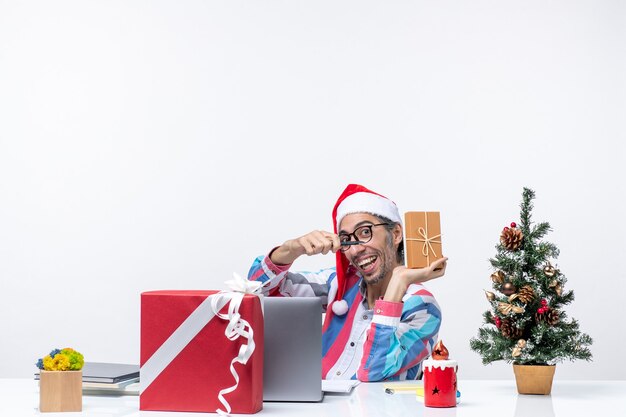 パッケージ感情クリスマスの仕事の休日のオフィスを保持している彼の職場に座っている正面図の男性労働者