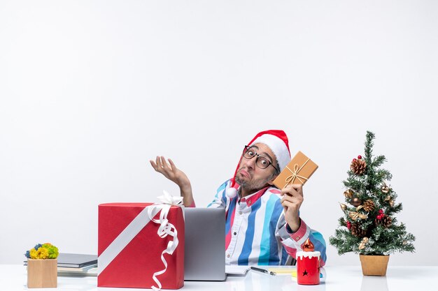 Вид спереди мужчина-работник, сидящий на своем рабочем месте, держа пакет человека, рождественская работа, праздник эмоций, офис