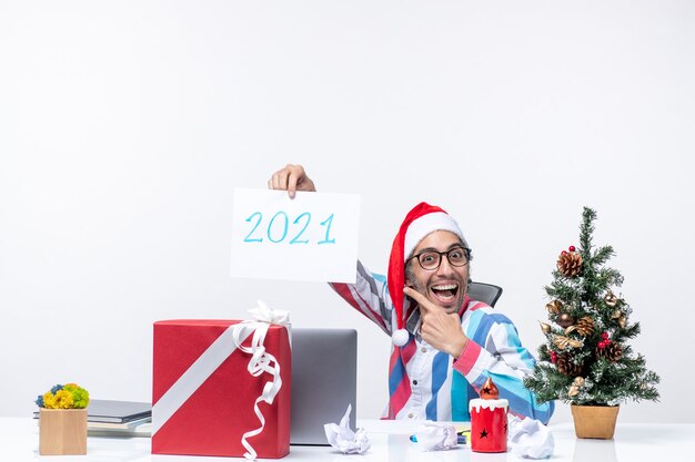 Front view male worker sitting in his working place holding paper sheet with number 2021, new year concept