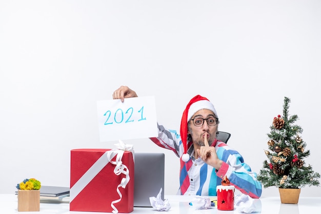 Вид спереди мужчина-работник сидит на своем рабочем месте и держит лист бумаги с номером 2021, новогодняя концепция