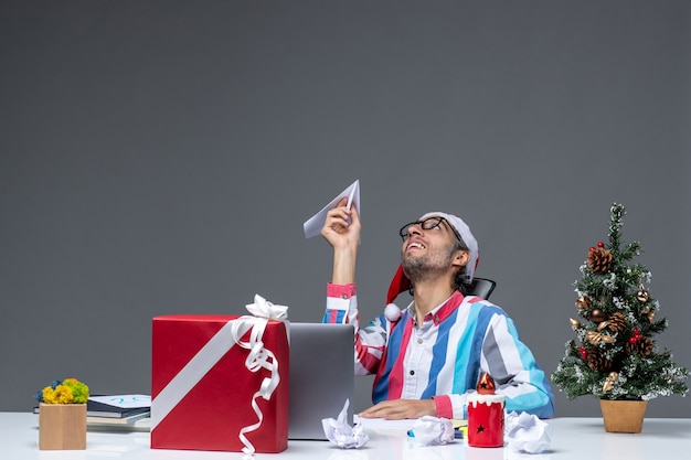 Lavoratore maschio di vista frontale che si siede nel suo posto di lavoro che gioca con l'aeroplano di carta