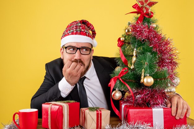 Front view male worker sitting behind his working place with presents on yellow desk office color job xmas new year gift