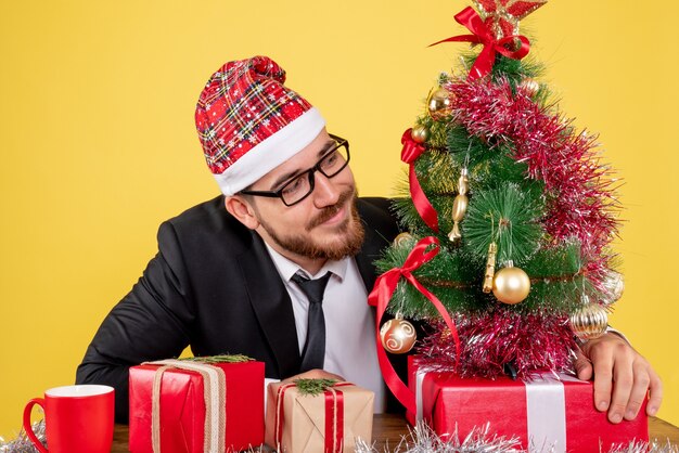 Front view male worker sitting behind his working place with presents on a yellow 