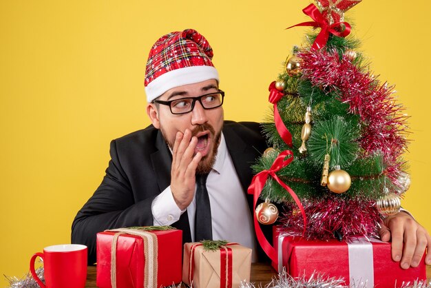 Front view male worker sitting behind his working place with presents on the yellow 