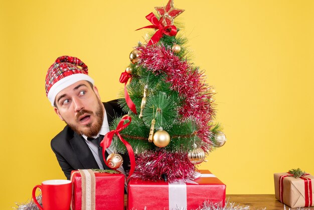 Front view male worker sitting behind his working place with presents on yellow 