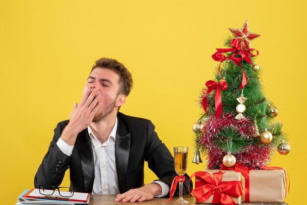 Front view male worker sitting behind his working place yawning on yellow 