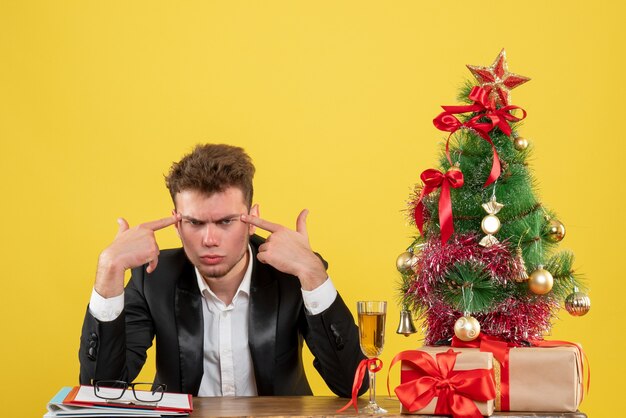 Front view male worker sitting behind his working place on yellow desk color emotion office job new year xmas