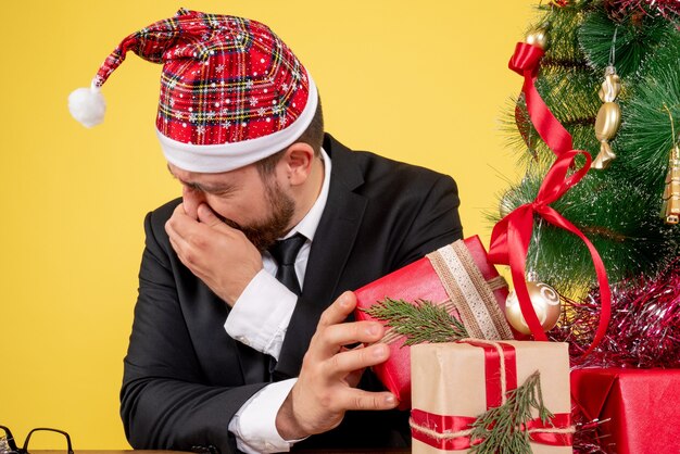 Front view male worker sitting and holding presents on the yellow 