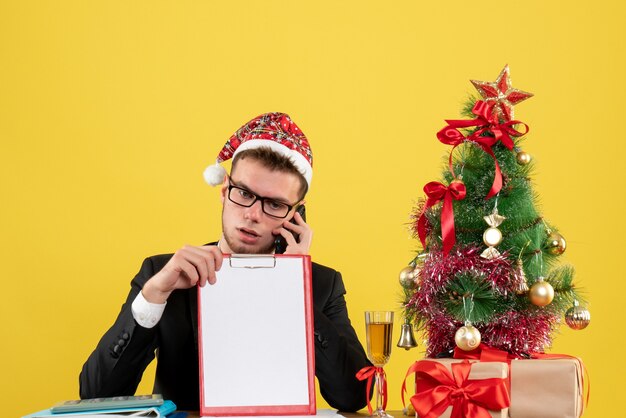 Front view male worker talking on the phone around little xmas tree and presents on light yellow 