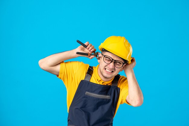 Front view male worker in uniform and helmet cutting his ear on blue 