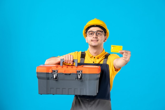 Front view male worker in uniform and helmet tool box and bank card on blue 