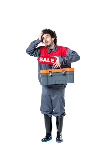 front view of male worker in uniform tools suitcase and sale on white wall